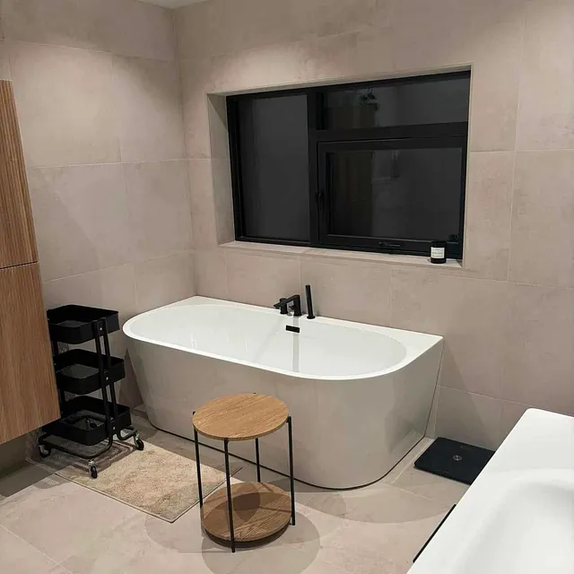 Stort badekar foran vindu, med sorte detaljer og minimalistisk innredning.