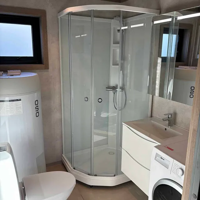 Bad med dusjkabinett, servant, toalett, varmtvannsbereder og vaskemaskin.